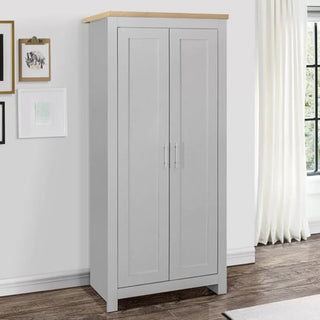 A tall CHOICEWARDROBE Highland 2 Door Wardrobe in grey with an oak top (79cm wide) stands against a white wall. Silver handles, framed pictures, and a window with white curtains complement this compact bedroom storage design.