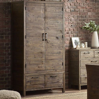 The CHOICEWARDROBE Homer Wooden Wardrobe features a rustic pine finish, metal handles, two doors, and two drawers, creating an industrial look beside a matching dresser against a brick wall for modern loft interiors.