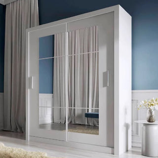 The CHOICEWARDROBE Ionia 2 Door Mirrored Sliding Wardrobe in matt white (180cm wide) stands against a blue and white wall, reflecting a bench. Beige curtains frame the area, while a small round table with flowers adds charm nearby.