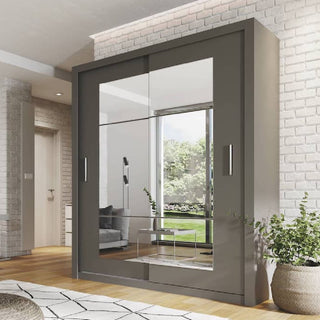 A modern bedroom features the CHOICEWARDROBE Ionia Mirrored Sliding Door Wardrobe (2 doors, 180cm, grey frame) against light brick walls, wood flooring, a patterned rug, and a green plant by the window overlooking a lawn.