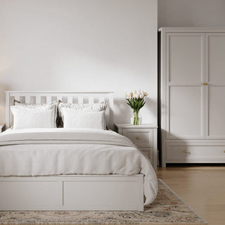 A neatly made bed with white bedding is centered in a minimalist bedroom. White nightstands with gold knobs and tulips sit beside the bed. The CHOICEWARDROBE Iowa 2 Door Wardrobe in white with gold handles provides extra storage on the right.