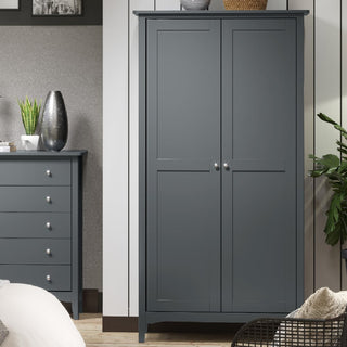 The CHOICEWARDROBE Kamuy 2 Door Wardrobe in midnight blue, featuring a hanging rail and storage shelf, stands beside matching furniture, providing modern bedroom storage against neutral walls with decorative plants and a vase.