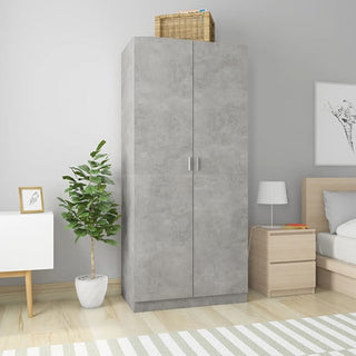 The CHOICEWARDROBE Kaylor 2 Door Wardrobe in a concrete effect finish stands against a light gray bedroom wall. A wicker basket is on top, with a potted plant, nightstand, white cabinet, framed picture, and striped rug nearby.
