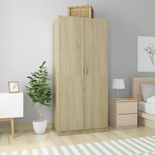 The CHOICEWARDROBE Kaylor Sonoma Oak 2 Door Wardrobe stands against a gray wall with a wicker basket on top. Nearby are a bedside table, bed with white bedding, potted plant, framed art, and light wood flooring.