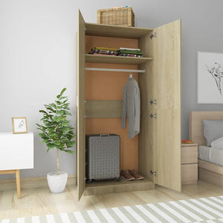 The CHOICEWARDROBE Kaylor Sonoma Oak 2 Door Wardrobe stands open, showing shelves with clothes, a hanging shirt, suitcase, and brown shoes. A wicker basket sits on top. Nearby are a plant, nightstand, and bed in the neat bedroom.