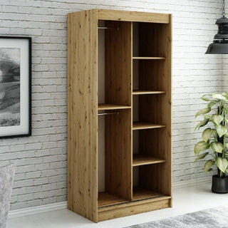 The CHOICEWARDROBE Laconia Mirrored Wardrobe—100cm in black and oak with 2 sliding doors, full-length mirror, and smooth glide tracks—stands against a white brick wall beside a framed picture, potted plant, and black hanging light.