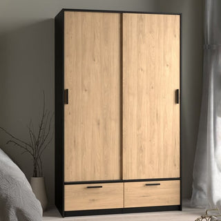 The CHOICEWARDROBE Liston 2 Door Sliding Wardrobe in black & oak finish with 2 drawers and black handles is placed against a light wall beside a bed and window with sheer curtains, offering modern storage.