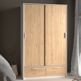 The CHOICEWARDROBE Liston 2 Door Sliding Wardrobe with Drawers in oak and white provides compact modern storage with smooth sliding doors and dual bottom drawers, perfect beside a bed near a window with sheer curtains.