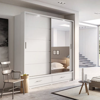 The CHOICEWARDROBE Lyra 2 Door Sliding Wardrobe features a matte white finish, large mirrored door, LED lighting, and two bottom drawers. The room includes a chair, small round table, partial bed view, and stairs.
