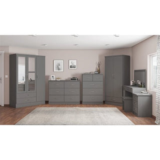 A modern bedroom features the CHOICEWARDROBE Mack 2 Door Wooden Wardrobe in graphite grey, offering sleek storage with a hanging rail and bottom drawer. The room includes a large gray rug, wooden floor, light walls, and framed art above the dressers.