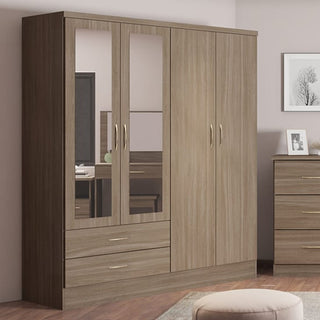 The CHOICEWARDROBE Mack 4 Door Mirrored Wardrobe in rustic oak offers spacious bedroom storage with two full-length mirrored doors, two drawers, and a stylish finish—perfect against a beige wall beside a chest of drawers and framed art.