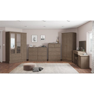 A bedroom features wooden furniture, including the CHOICEWARDROBE Mack Mirrored Wardrobe in walnut with full-length mirrors, two dressers, a vanity desk with a mirror, a beige rug and pouf on the floor, and two framed pictures on the light wall.