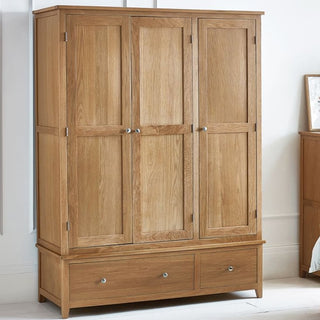 The CHOICEWARDROBE Macon 3 Door Solid Oak Wardrobe features a natural wood finish, classic panelled doors, double drawers for storage, and simple metal knobs—perfect against a light-colored wall.