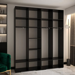 The CHOICEWARDROBE Madrid 4 Door Wardrobe in black fluted design with gold circular handles and sliding storage stands against a light wall. On the left, a green chair and bookshelf are partially visible.