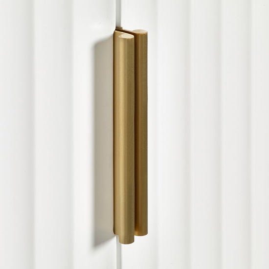 Brushed gold handle on a fluted matt white wardrobe door.