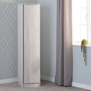 A CHOICEWARDROBE McGowan 40cm Wooden Single Door Wardrobe in Urban Snow Oak Finish stands in a sunlit room with light blue walls, patterned wallpaper, and gray curtains—perfect compact hanging storage for bedrooms or hallways.