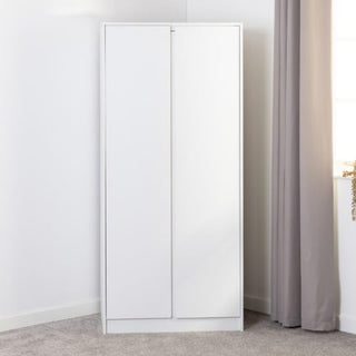 The CHOICEWARDROBE McGowen 2 Door Wooden Wardrobe in 80 cm matt white finish stands in the corner, offering modern storage with shelves and a hanging rail, near a window with a gray curtain and light gray carpet underneath.