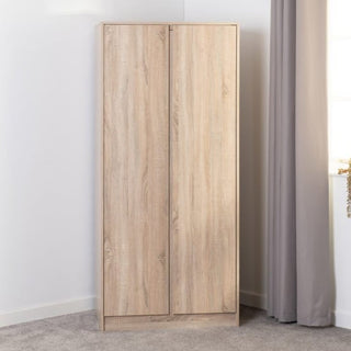 A CHOICEWARDROBE McGowen 2 Door Wooden Wardrobe in 80cm Sonoma Oak finish stands by a window with grey curtains, offering compact bedroom storage with a hanging rail and shelf in its light wood design.