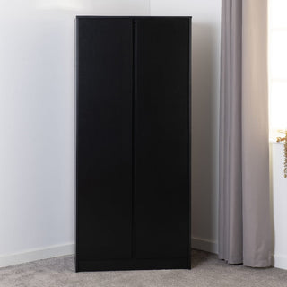 The CHOICEWARDROBE McGowen 80cm Black Wooden 2 Door Wardrobe stands in the corner of a carpeted room with white walls and light gray curtains, adding compact modern storage with its hanging rail and shelf.