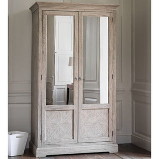 The CHOICEWARDROBE Mestiza 2 Door Wooden Wardrobe (111.5cm, Natural Finish) features rustic mirrored doors, carved detailing, and a solid frame. A white wastebasket on the left adds practicality from Furniture in Fashion.