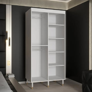 The CHOICEWARDROBE Millwall 100cm White Marble Effect 2 Door Sliding Wardrobe, with ribbed panels, gold handles, and a compact design, stands against a dark wall in a modern bedroom.