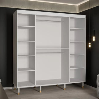 The CHOICEWARDROBE Millwall 200cm White Wooden Sliding Door Wardrobe features fluted panels, gold handles, and elevated legs, offering stylish bedroom storage against a dark wall in a modern space with pendant lights.