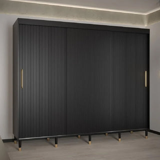 The CHOICEWARDROBE Millwall 250cm Black Wooden Sliding Door Wardrobe with fluted panels, gold handles, and a luxury storage system stands against a light wall in a modern room with minimal decor and wood flooring.