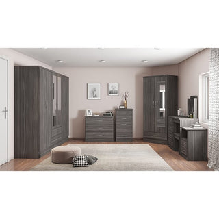 A modern bedroom features the CHOICEWARDROBE Modara 230cm 6 Door Mirrored Wardrobe in dark grey oak wood grain finish, complemented by dressers, a vanity, a corner unit, framed pictures, and a pouf on a beige rug over wooden floors.