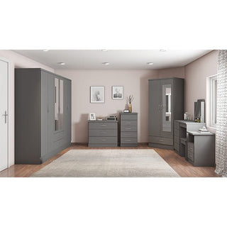 A modern bedroom with light pink walls, wood flooring, and a large rug features the CHOICEWARDROBE Modara 230cm grey 6 door wardrobe with mirrors and drawers, framed art above dressers, and natural light entering from the right.
