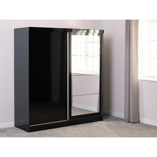 The CHOICEWARDROBE Modora Black High Gloss 2 Door Sliding Wardrobe with Full-Length Mirror stands against a light wall, next to a window with gray curtains on a light gray carpeted floor.