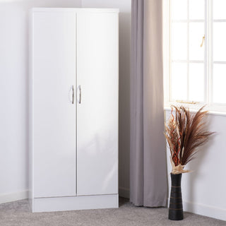 The CHOICEWARDROBE Modora White High Gloss 2 Door Wardrobe, featuring a sleek gloss front, stands on a grey carpet near a window with grey curtains. A black vase with dried decorative plants is placed beside the wardrobe.