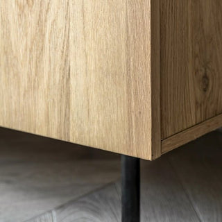 Close-up of the CHOICEWARDROBE Nairo Natural Oak Wooden Wardrobe’s corner with a natural grain finish, standing on black metal legs. Gray tiled flooring is visible underneath, reflecting its modern Scandinavian design.