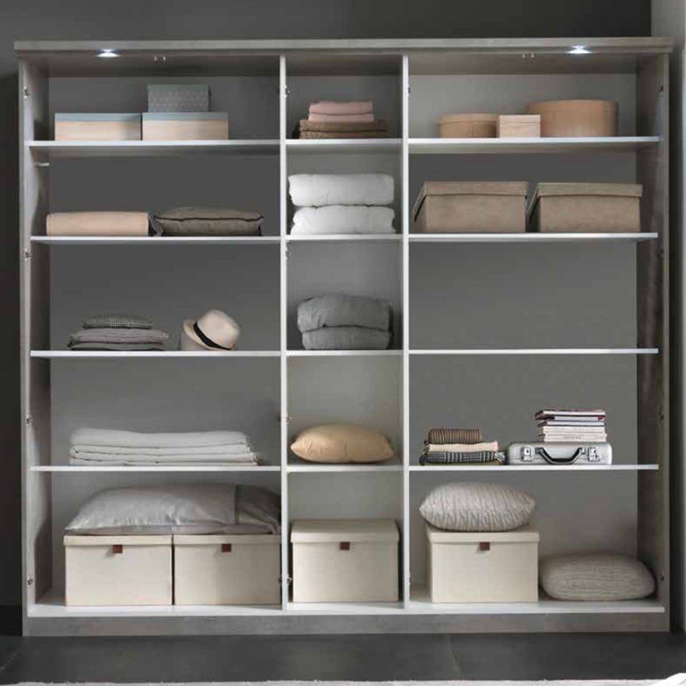 Wardrobe interior with shelves holding folded clothes, storage boxes, pillows, and a hat.