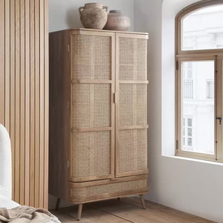 The CHOICEWARDROBE Nixa Oak Rattan Wooden Wardrobe (90 cm, 2 Door + 1 Drawer) features cane front panels and solid wood legs. Two ceramic vases sit atop it as sunlight streams in, making it a stylish Boho Scandi bedroom storage solution.