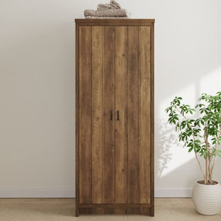 The CHOICEWARDROBE Nolan Knotty Oak 2 Door Wardrobe with rustic wooden design and black handles stands against a white wall. A folded towel is on top, and a potted green plant rests to the right on a light-colored carpet.
