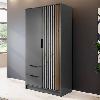 The CHOICEWARDROBE Norco 2 Door Hinged Wardrobe in matt black with oak slatted design features two lower drawers, a hinged door above, and vertical slats on the right, standing against a brown wall in a bright room.