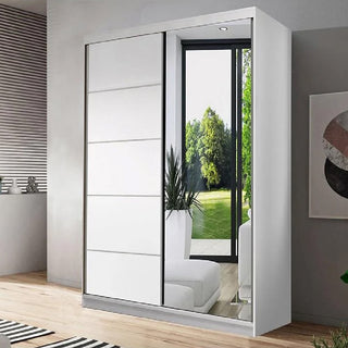 The CHOICEWARDROBE Norvik 2 Door Sliding Wardrobe in matt white (120cm) features one solid and one mirrored door, perfectly reflecting light and greenery in a bright bedroom with wooden floors and minimalist decor.