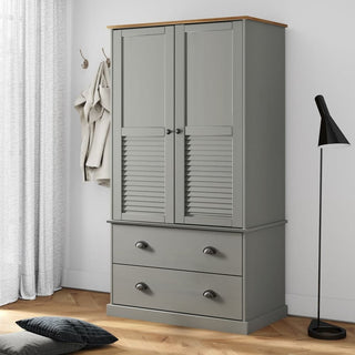 A CHOICEWARDROBE Norwyn Grey Wooden Wardrobe with 2 drawers, oak top, and louvre doors stands against a white wall, surrounded by a floor lamp, curtain, wall hooks with coat and bag, plus a pillow on the wooden floor.