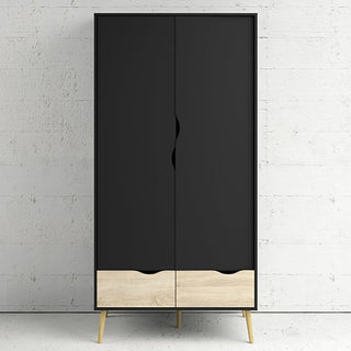 The CHOICEWARDROBE Nuvell Black & Oak 2 Door Wardrobe with Drawers stands against a white textured wall, elevated on four light wood legs for a modern minimalist look.