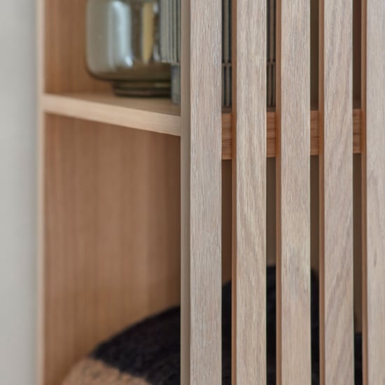 Natural oak open wardrobe with slatted back, showing glass jar and dark cushion.