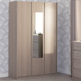 A CHOICEWARDROBE Palmyra 3 Door Mirrored Wardrobe in a 120cm Sonoma Oak finish stands by a geometric-patterned wall; its center door features a full-length mirror, with a dresser partly visible by the curtained window.