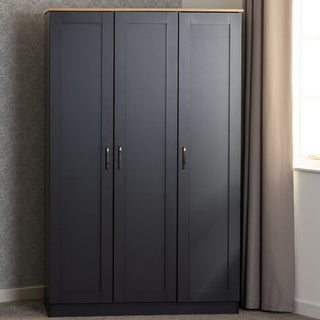 The CHOICEWARDROBE Parnu 3 Door Wooden Wardrobe in grey and oak finish, featuring a modern panelled design with hanging rail and shelving, provides stylish bedroom storage against patterned wallpaper by a window with beige curtains.