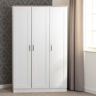 The CHOICEWARDROBE Parnu White & Oak Wooden 3 Door Wardrobe, a modern Scandinavian storage piece, stands against patterned wallpaper on the left and a window with beige curtains on the right. The floor is carpeted.