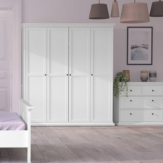 A bright bedroom featuring the CHOICEWARDROBE Paroya 4 Door Wardrobe in classic white, paired with a matching dresser and bed with a light purple blanket. Three pendant lamps, a framed picture, and a potted plant complete the decor.