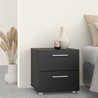 A black CHOICEWARDROBE Perkin bedside cabinet with silver handles from the 3 Piece Bedroom Furniture Set sits beside a bed. A beige vase and brown candle holder rest on top, with dried pampas grass in the corner.