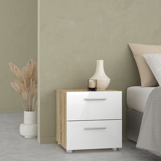 A modern bedroom showcases the CHOICEWARDROBE Perkin 3 Piece Set in white and oak—a minimalist bedside table beside a bed with beige bedding, topped with a white vase, brown glass, candle, and dried grasses in a ceramic vase nearby.