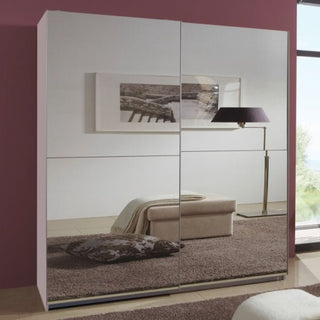 The CHOICEWARDROBE Quinn 2 Door Fully Mirrored Sliding Wardrobe (180 cm, Gloss White) complements a modern bedroom featuring a beige ottoman, patterned pillow, brown rug, framed wall art, and floor lamp by a large window.
