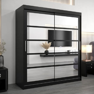 The CHOICEWARDROBE Reston Sliding Mirror Wardrobe (2 Doors, 180cm, Black Finish) reflects a wall-mounted TV, a floating shelf with dried plants in a vase, a lamp on a nightstand, and part of a sofa in a modern minimalist room.