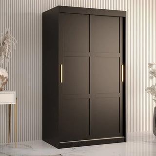 The CHOICEWARDROBE Rieti I 2 Door Sliding Wooden Wardrobe in black with gold handles and internal storage shelves (100cm wide) adds modern, space-saving storage against a striped wall, with decorative items on either side.