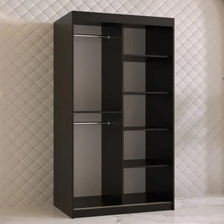 The CHOICEWARDROBE Rieti Wardrobe 100cm in black finish features 2 sliding doors with a mirror and gold handles, and is sleek bedroom furniture perfect for standing against a quilted white wall on a white tiled floor.